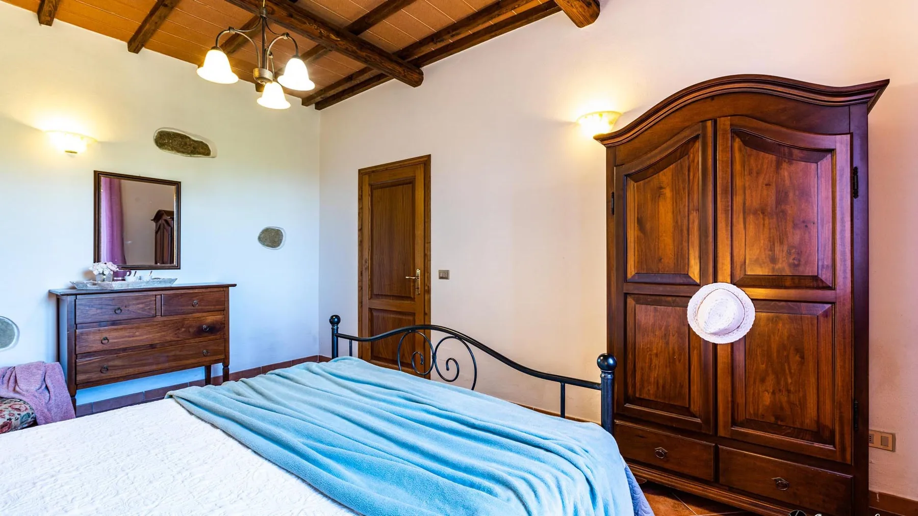 A bedroom with a wooden bed, a blue coverlet, and a large wardrobe.