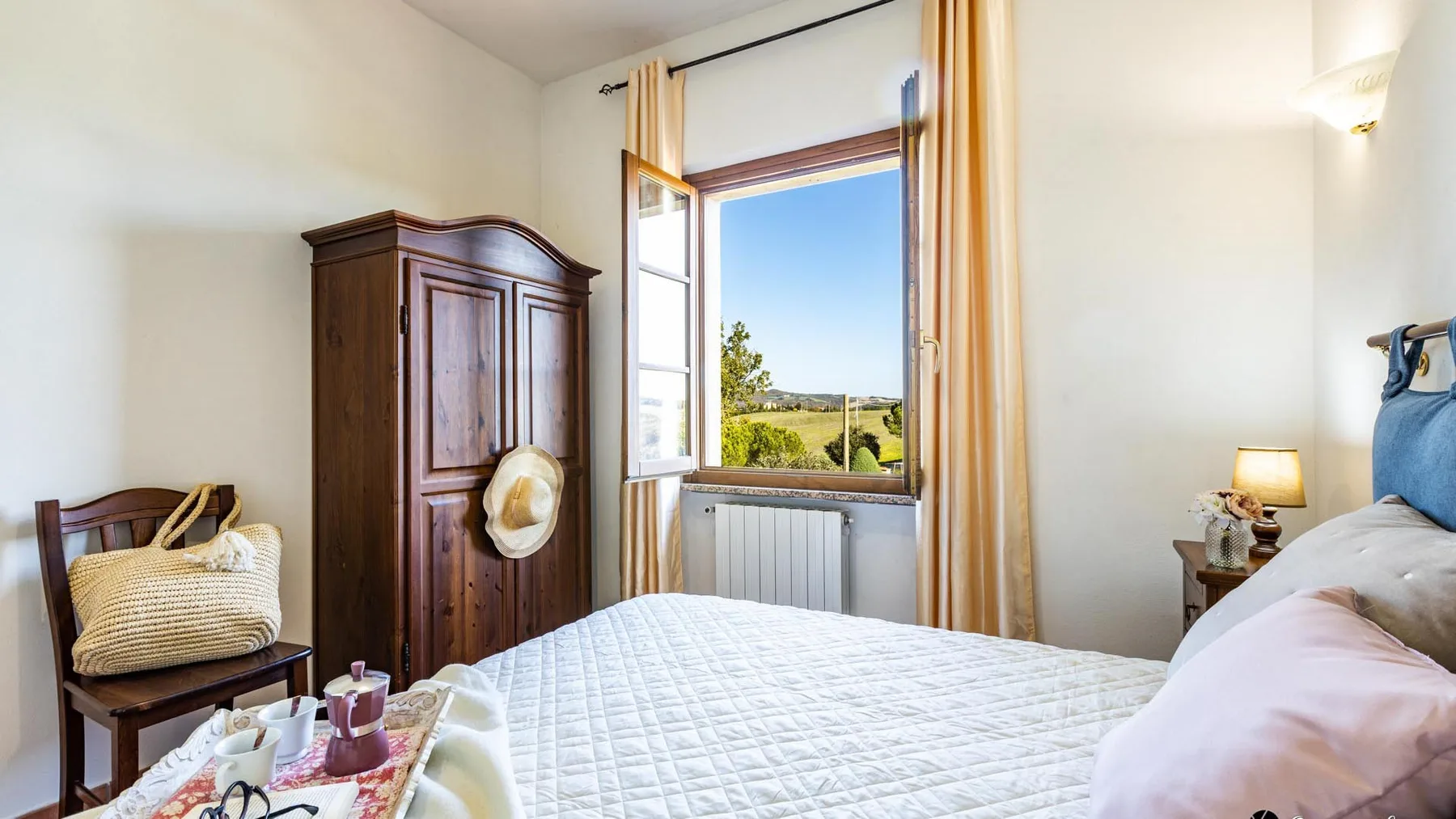 A bright bedroom with a large bed beside an open window overlooking greenery.