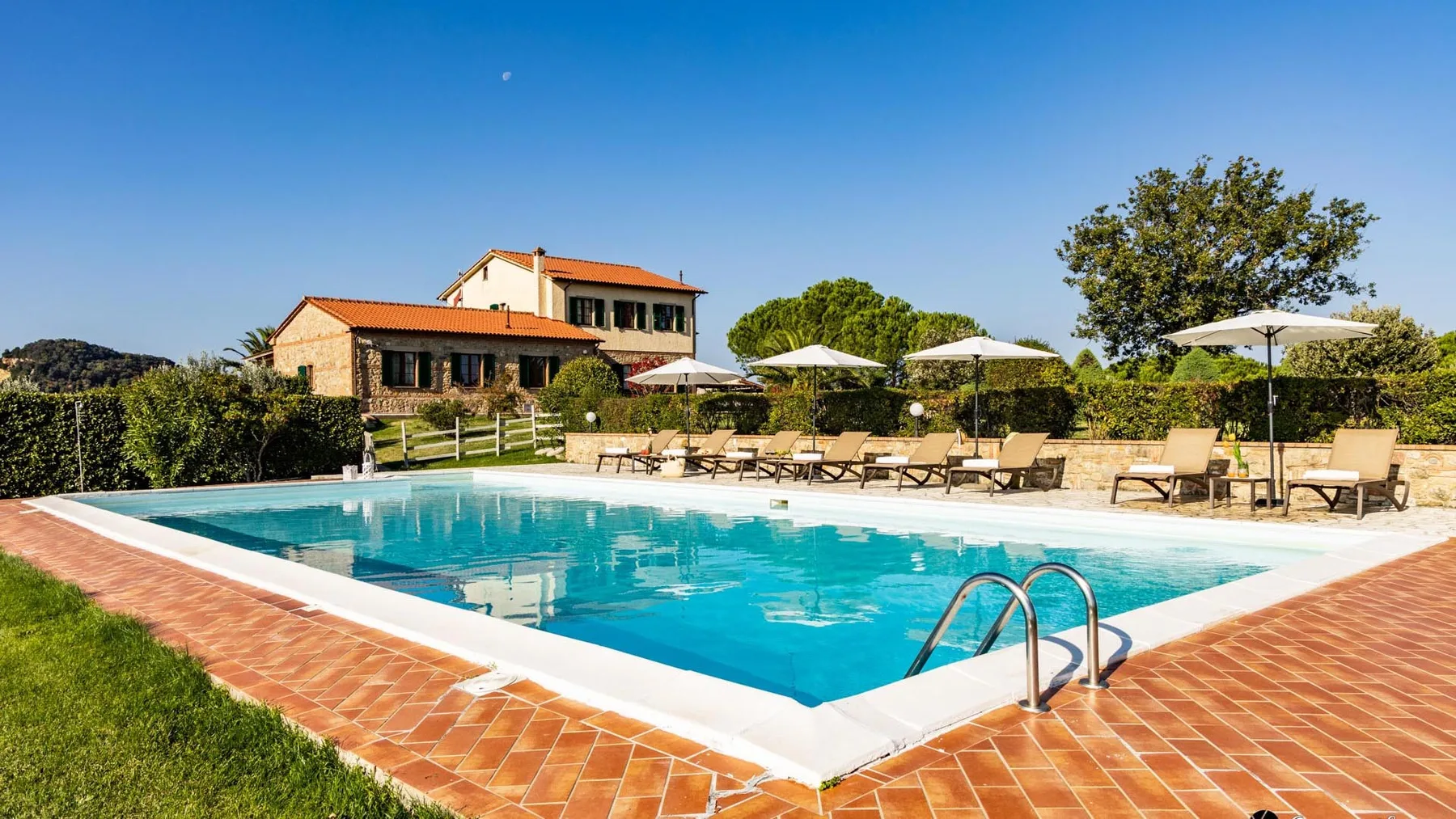 An outdoor swimming pool bordered by terracotta-colored paving and lounge seating.