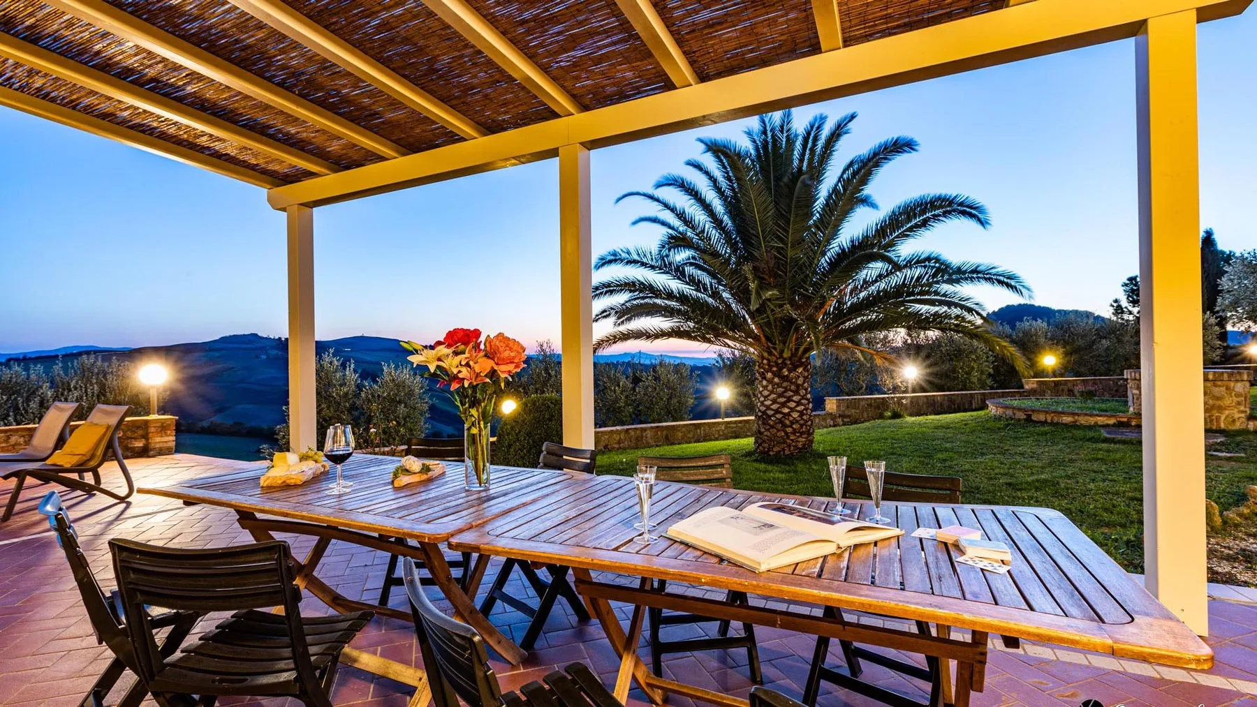 A covered outdoor dining area overlooks a garden with a palm tree.