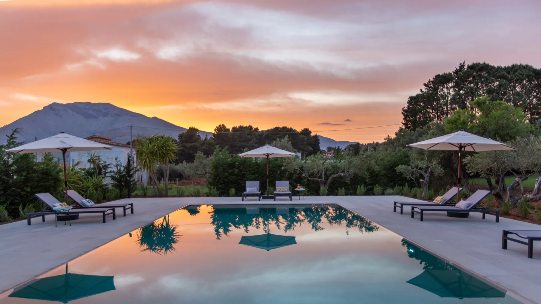 Una piscina al aire libre refleja el colorido atardecer junto a asientos para descansar.