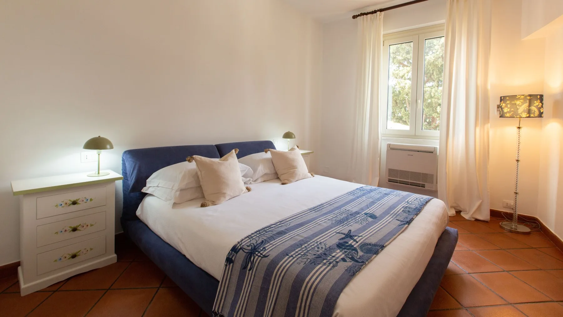 Un dormitorio con una cama vestida con ropa de cama blanca y detalles azules.