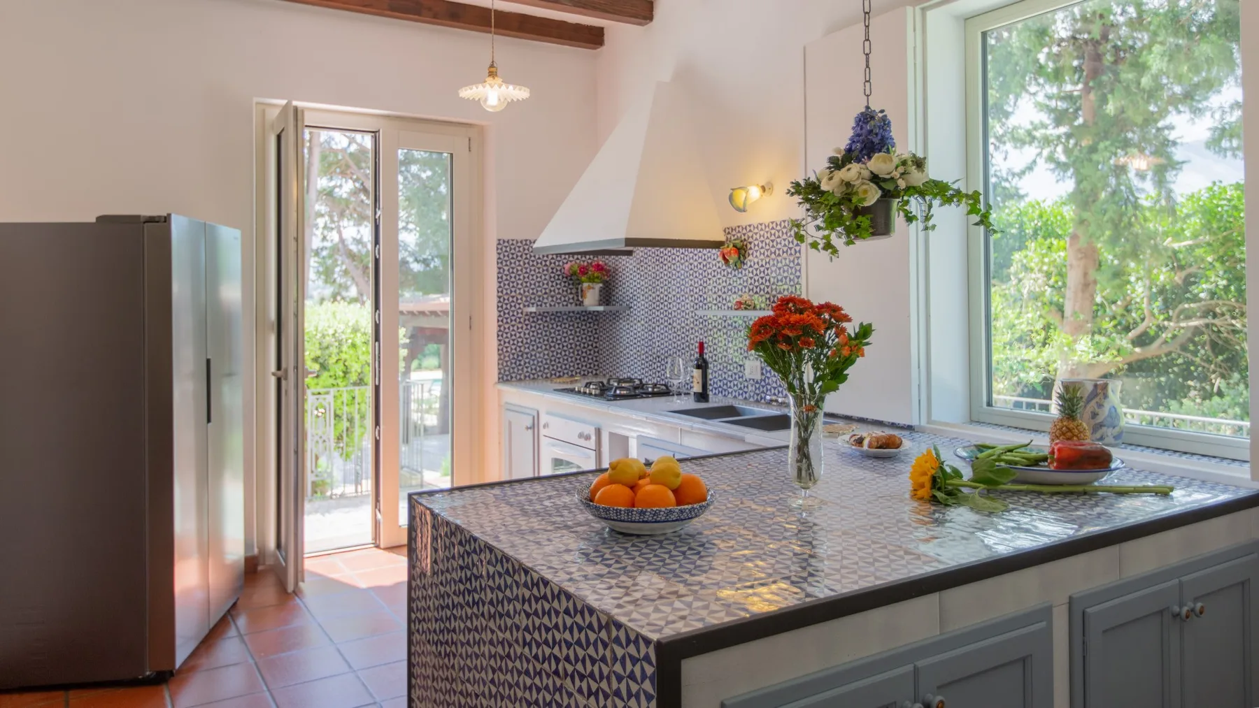 Una cocina luminosa con una isla de azulejos y grandes ventanas que dan a la vegetación.
