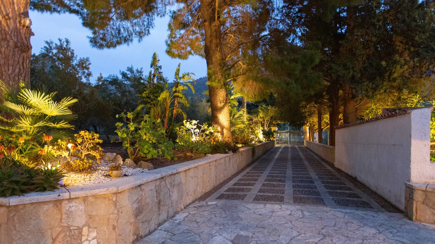 Un camino empedrado atraviesa jardines con árboles.