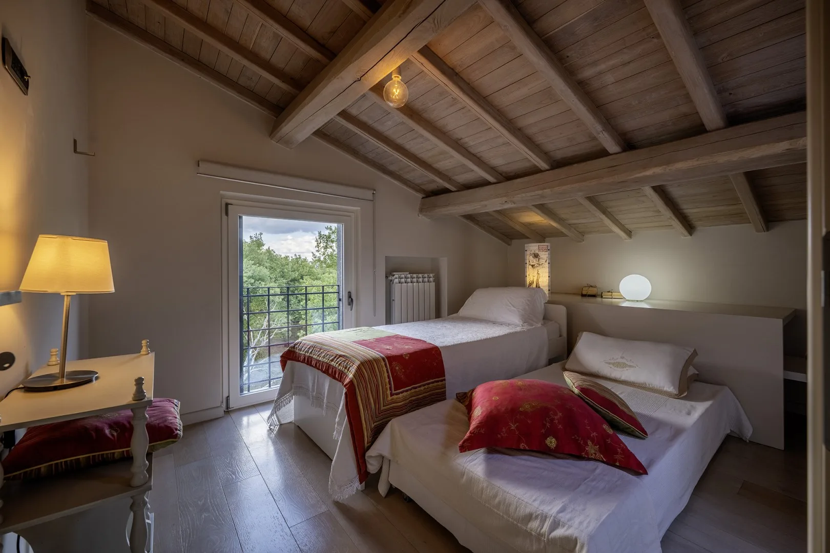 A bedroom with two beds, exposed wooden ceiling beams, and a glass door to a balcony.
