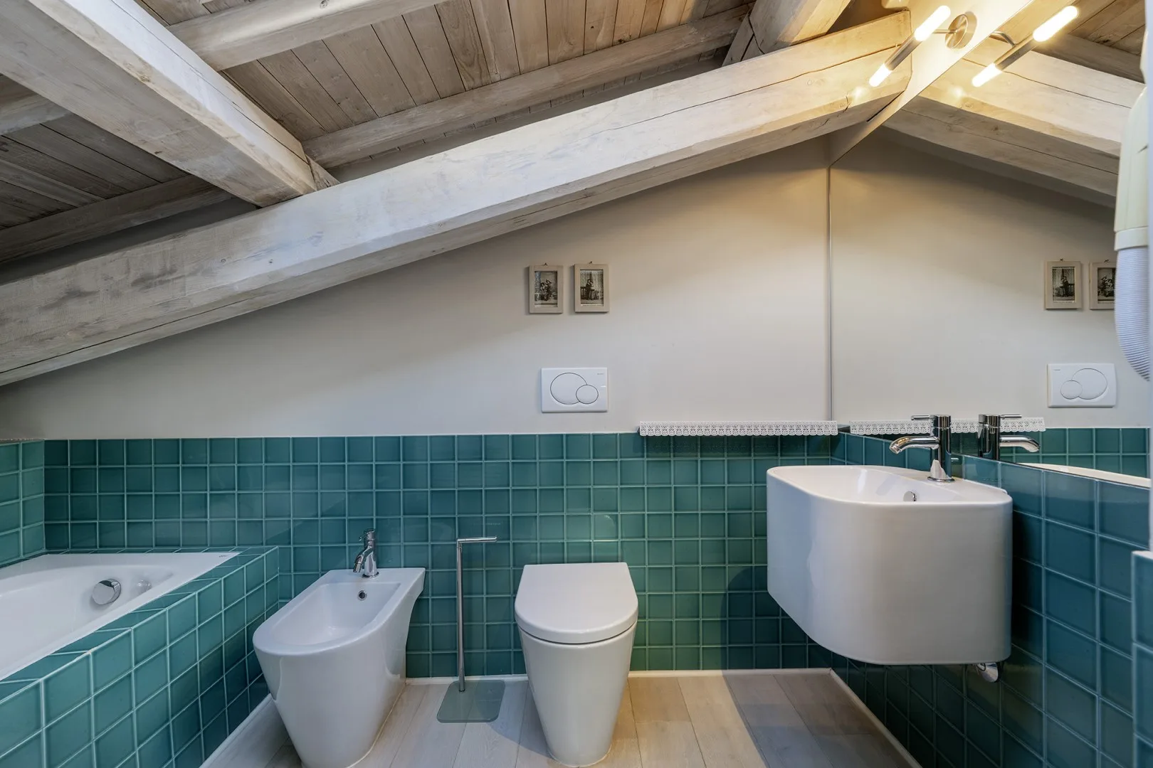 A bathroom with teal tiled walls, a bathtub, bidet, toilet, and sink.