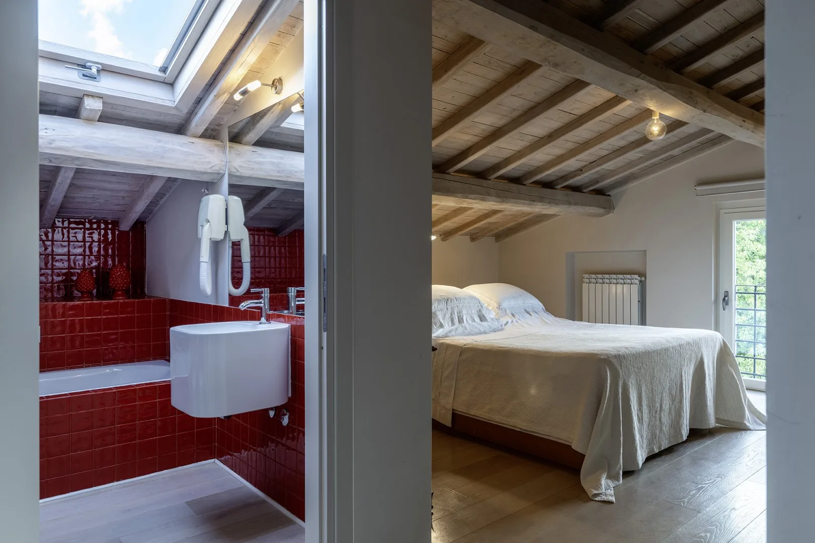 A bedroom with a white bed sits beside a bathroom with red tile.