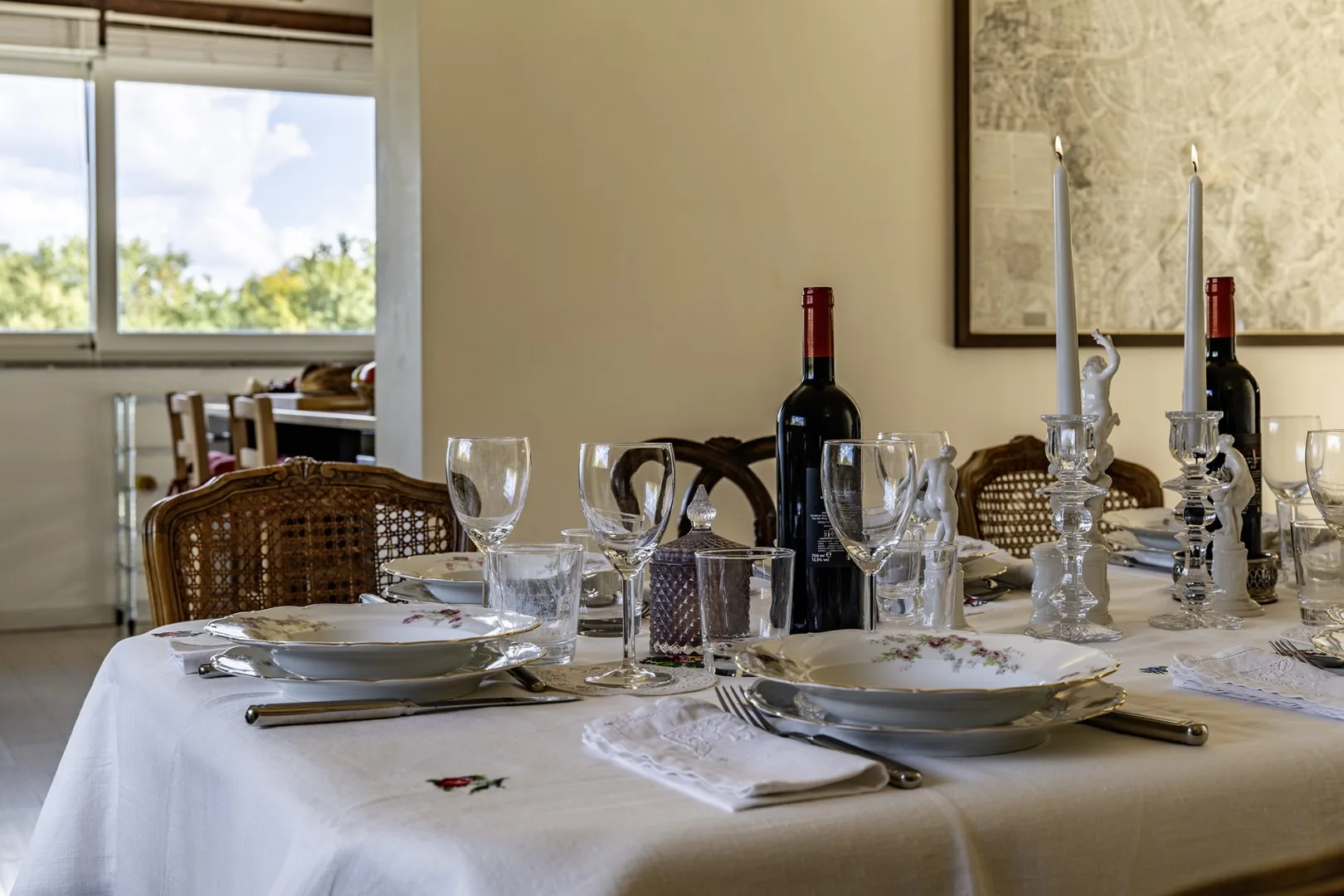 A dining table is set with plates, glassware, and wine bottles.