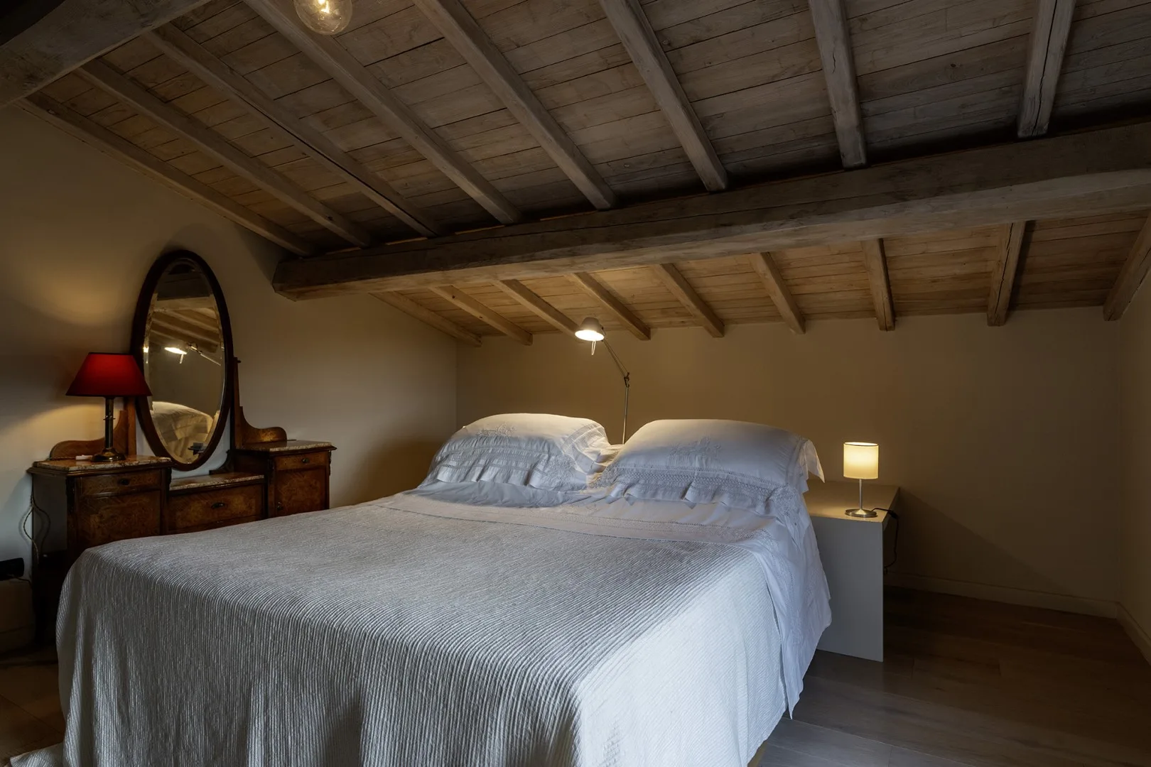 A bedroom with a bed beneath a sloped, exposed-beam ceiling.