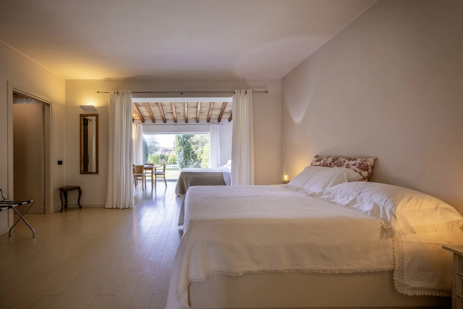 A bedroom with a neatly made bed and an open view to a bright adjoining space.