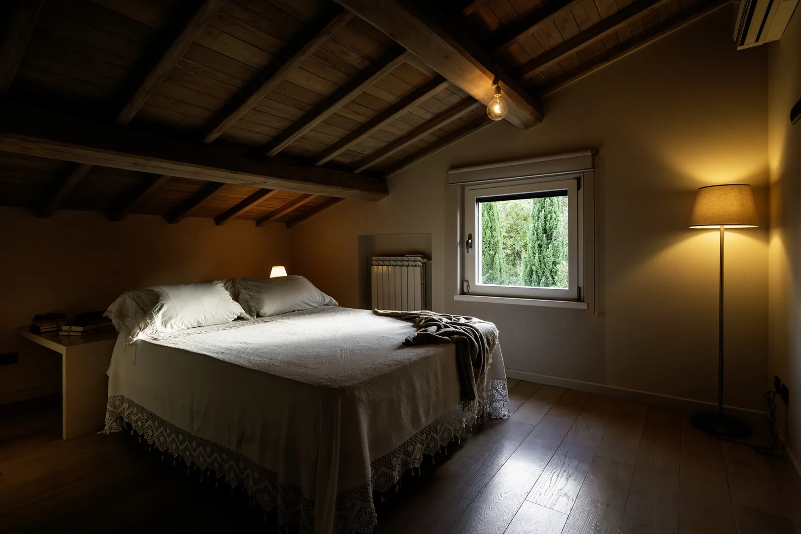 A bedroom with a bed beneath a sloped wooden ceiling and a window.