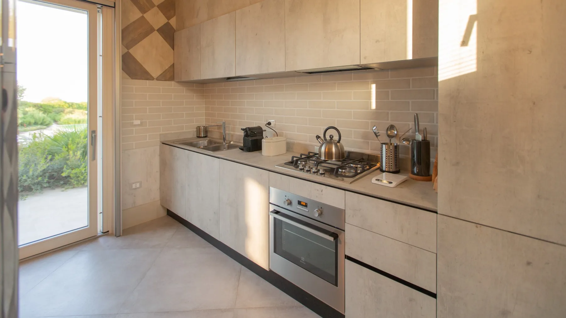 A modern kitchen with a built-in oven and a glass door opening outdoors.