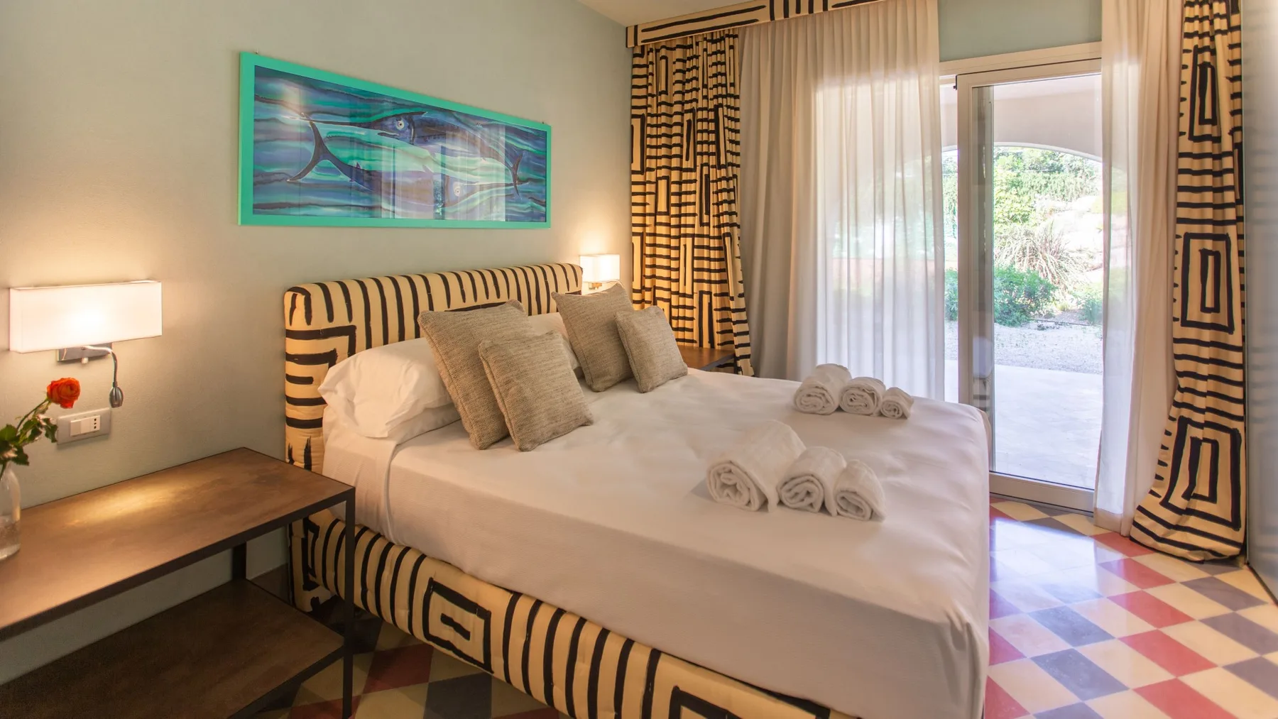 A bedroom with a neatly made bed and patterned curtains beside a glass door.