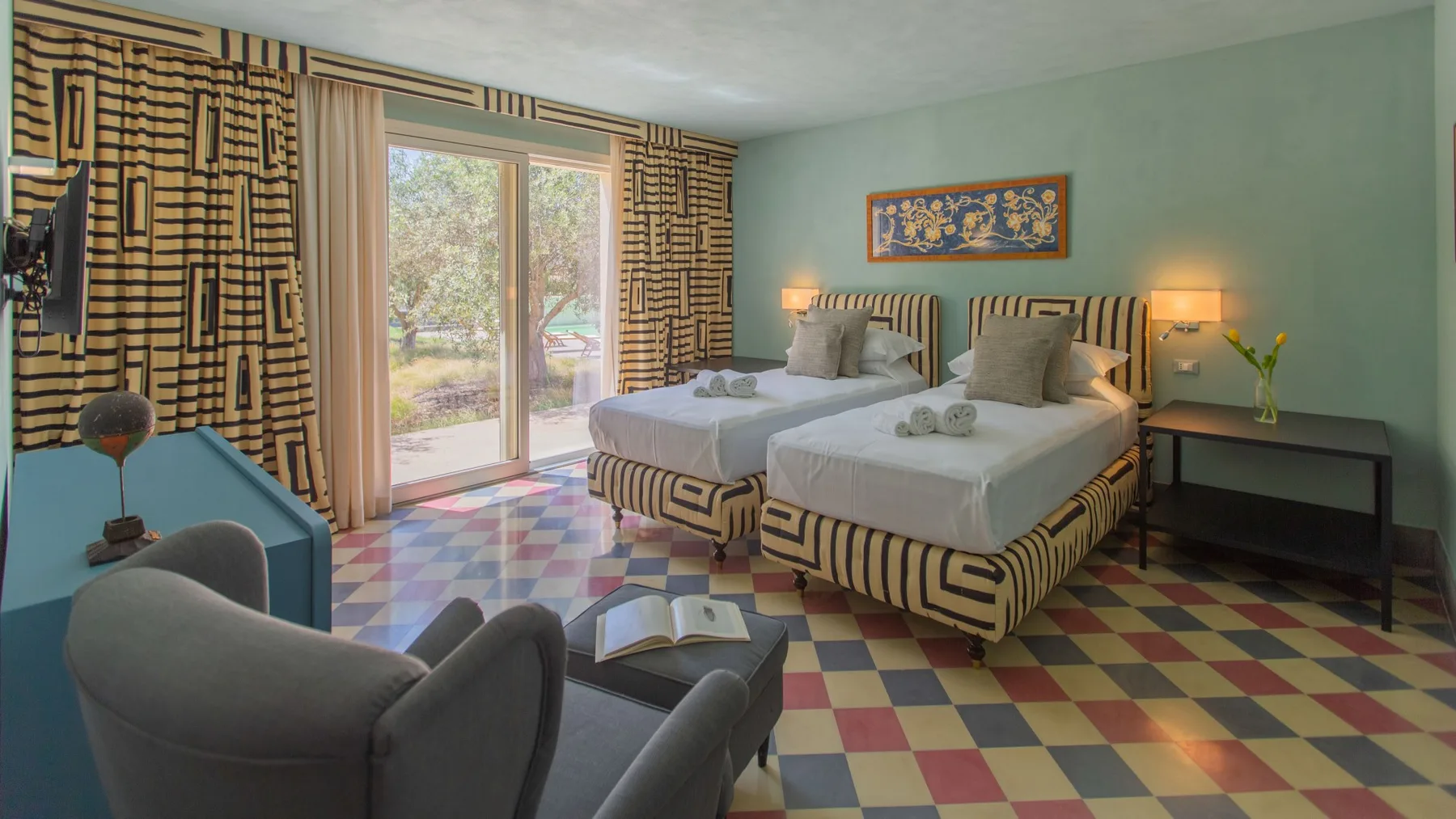 A bedroom with two beds, a seating area, and a glass door opening to greenery.