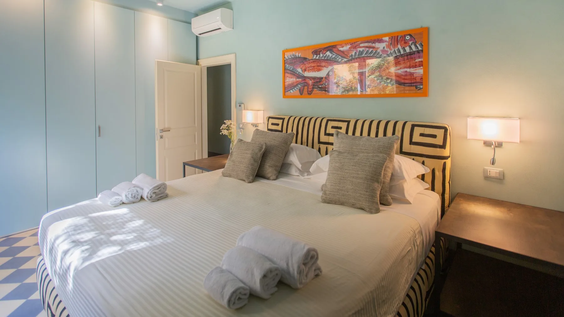 A bedroom with a large bed, bedside tables, and colorful artwork above the headboard.