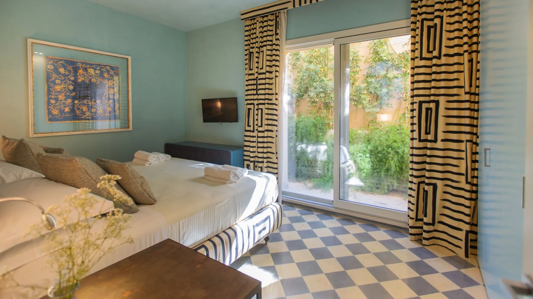 A bedroom with a large bed beside glass doors opening onto a garden.