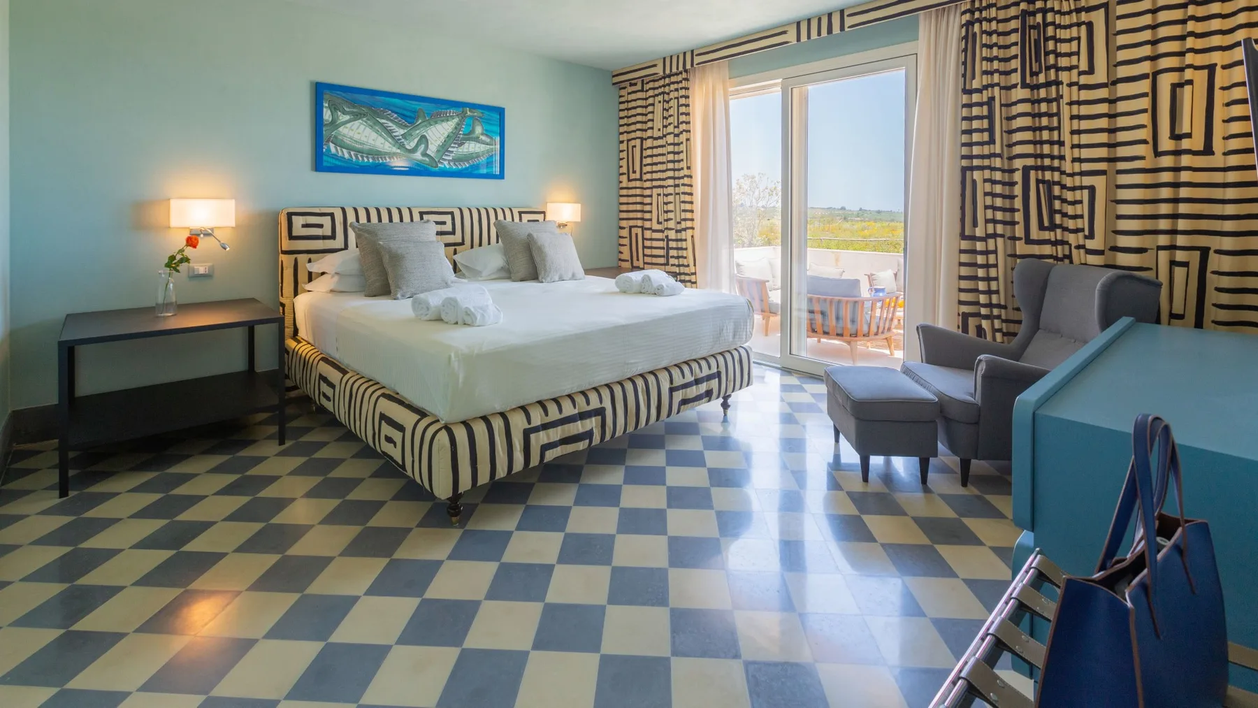 A bedroom with a large bed, patterned curtains, and seating beside glass doors.