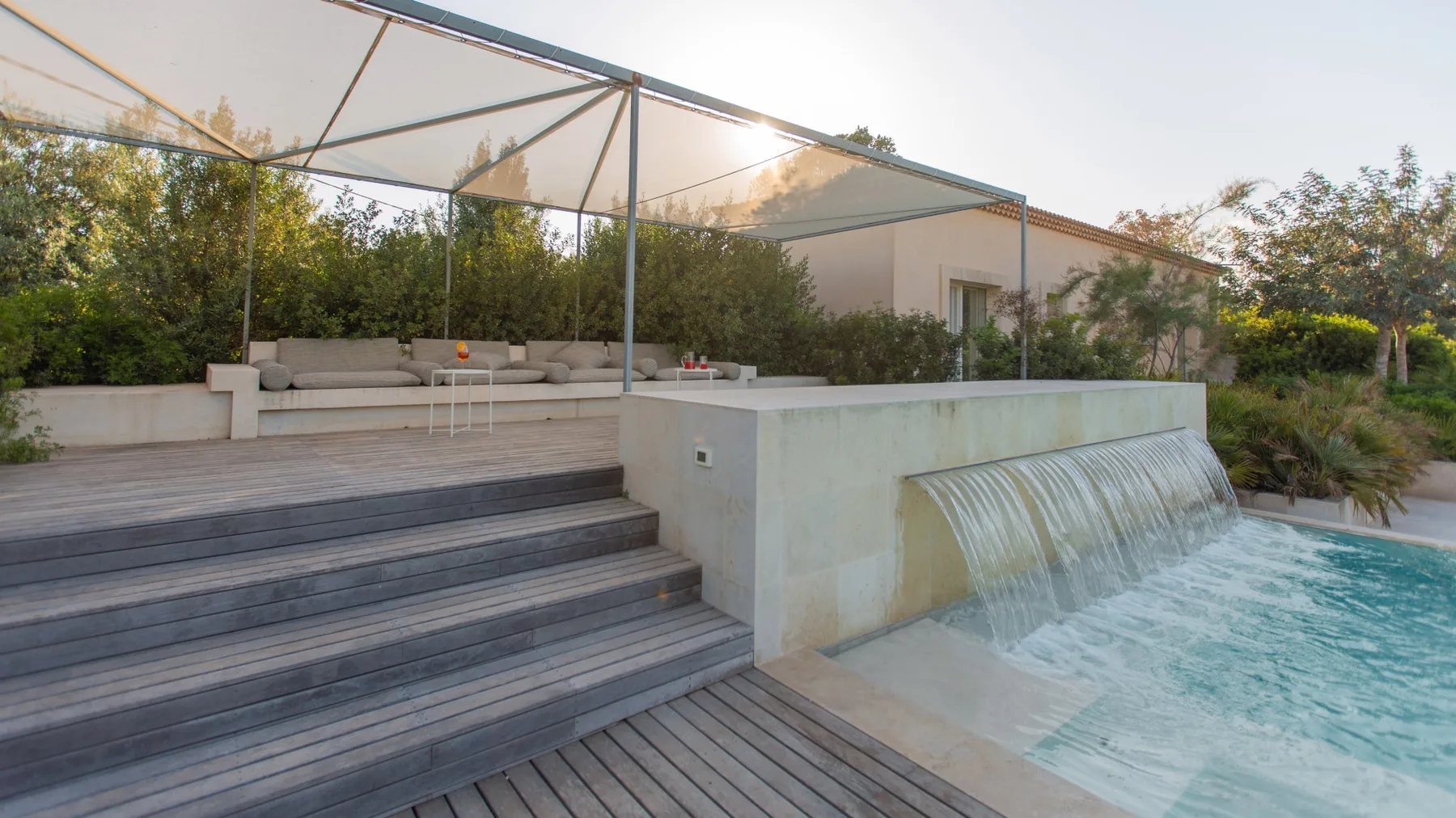 A swimming pool with a cascading water feature beside a shaded outdoor seating area.