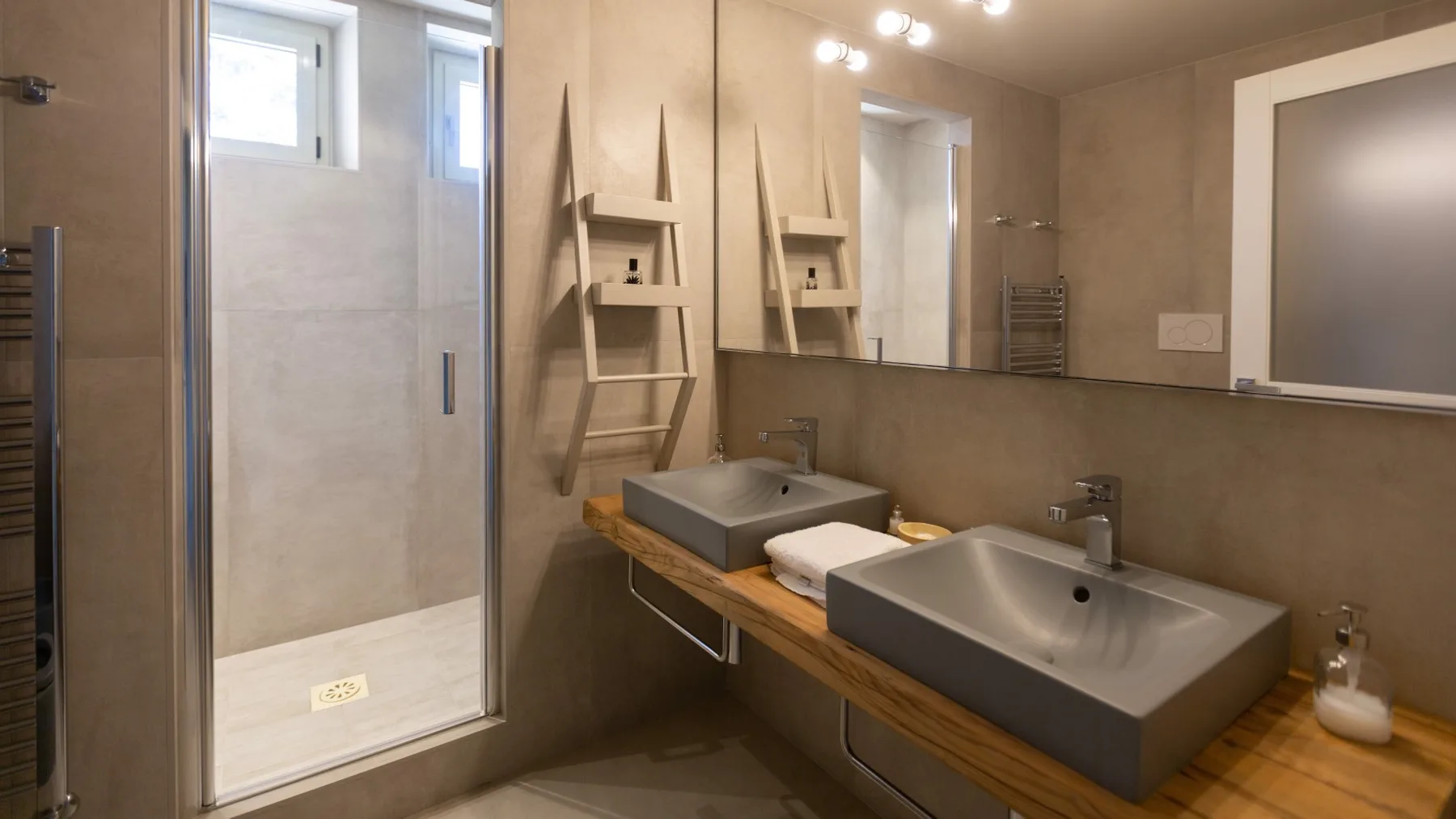 A bathroom with two sinks beneath a wide mirror and a glass shower.