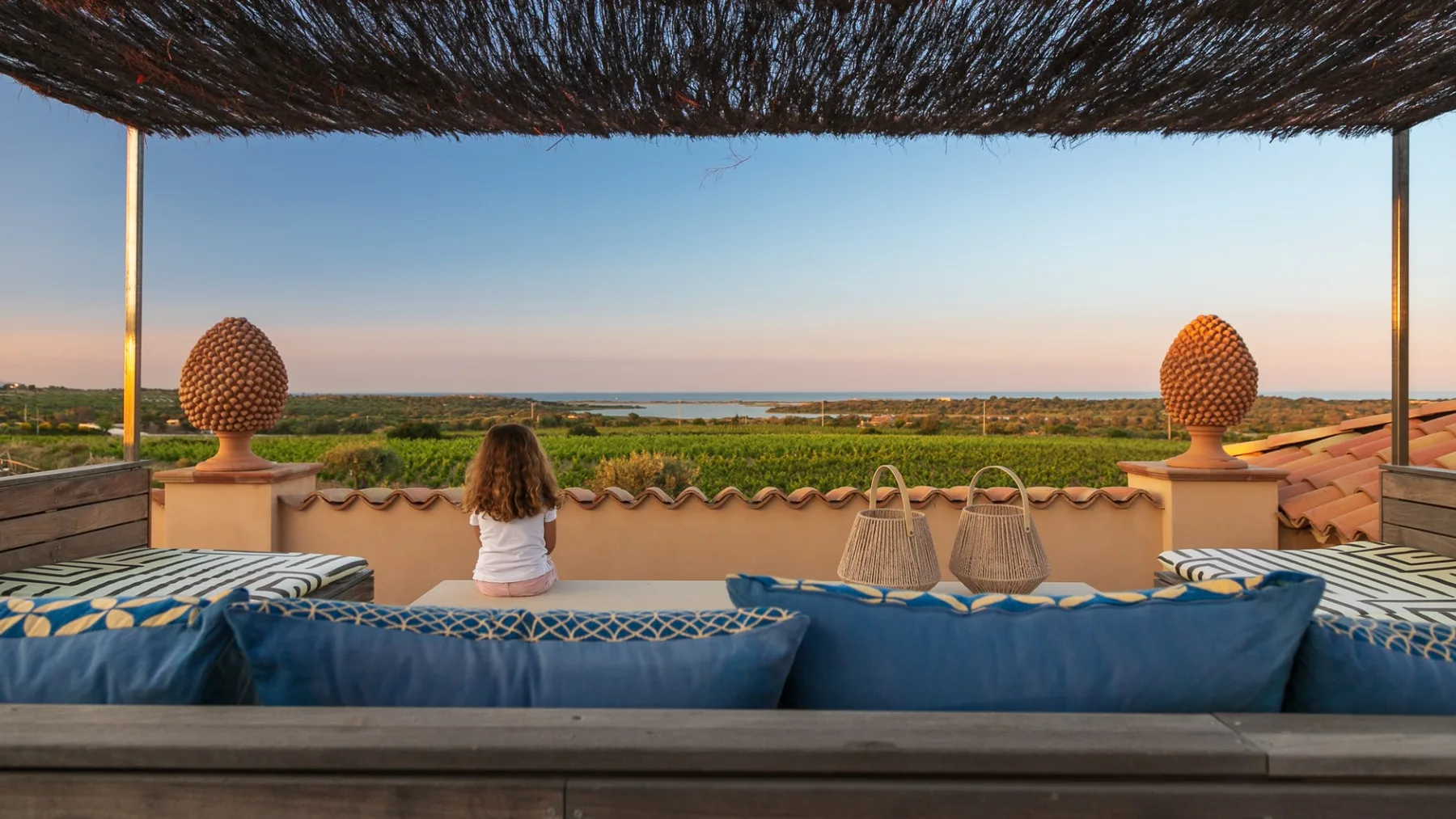 A shaded rooftop terrace overlooks the landscape and distant water, with blue seating along the edge.