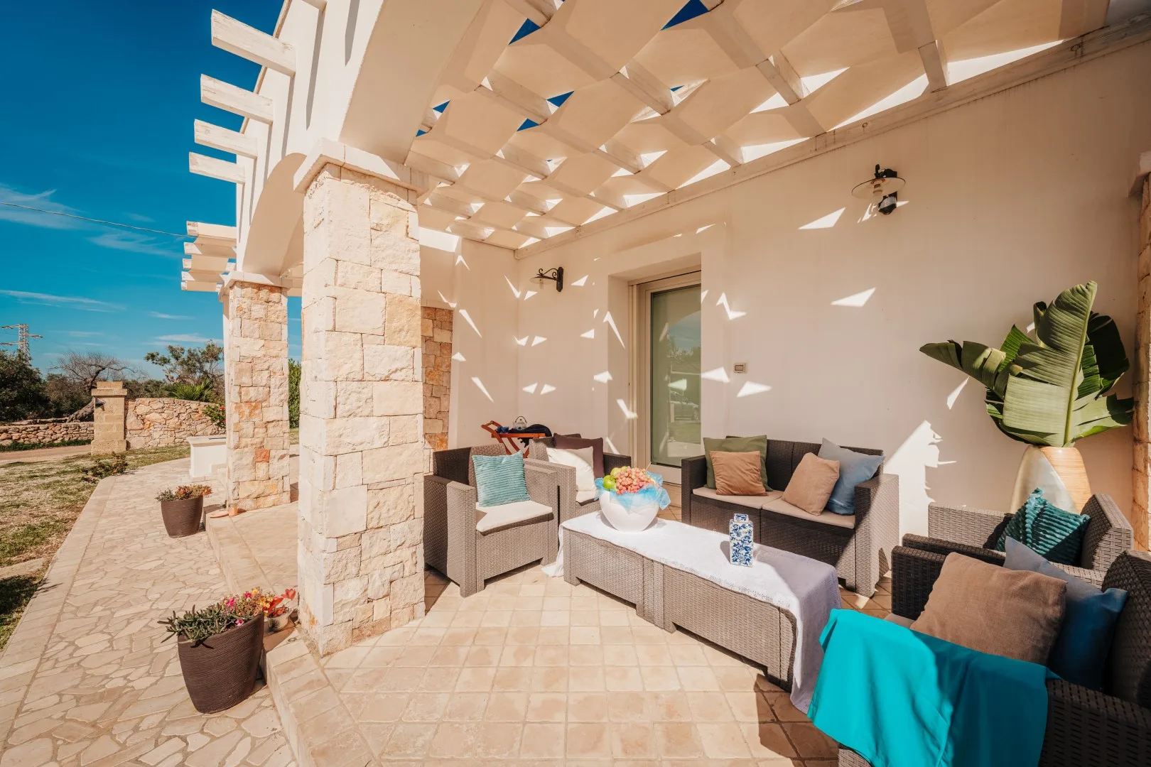 Una luminosa zona de estar en un patio exterior bajo una pérgola blanca.