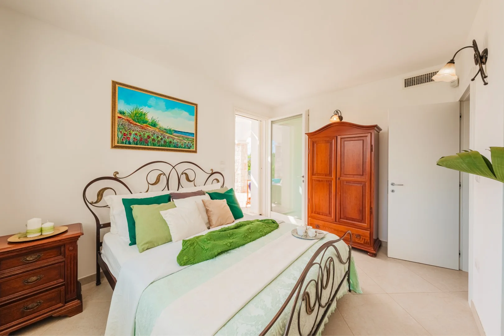 Un dormitorio luminoso con una cama de estructura metálica, ropa de cama colorida y un armario de madera.