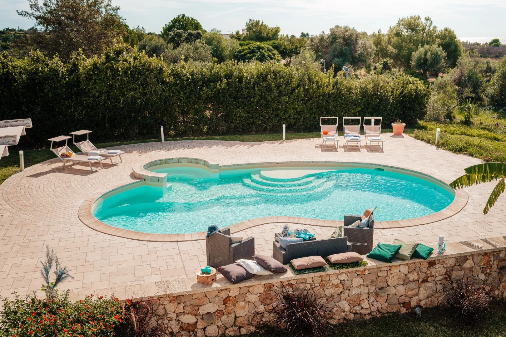 Una piscina al aire libre se encuentra en un patio pavimentado rodeado de vegetación.