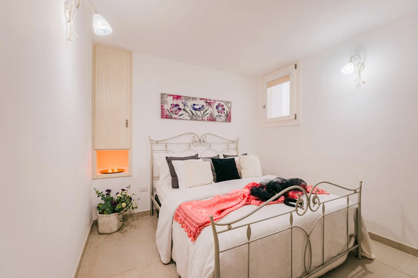 Un dormitorio con una cama de metal, ropa de cama colorida y una pequeña ventana.