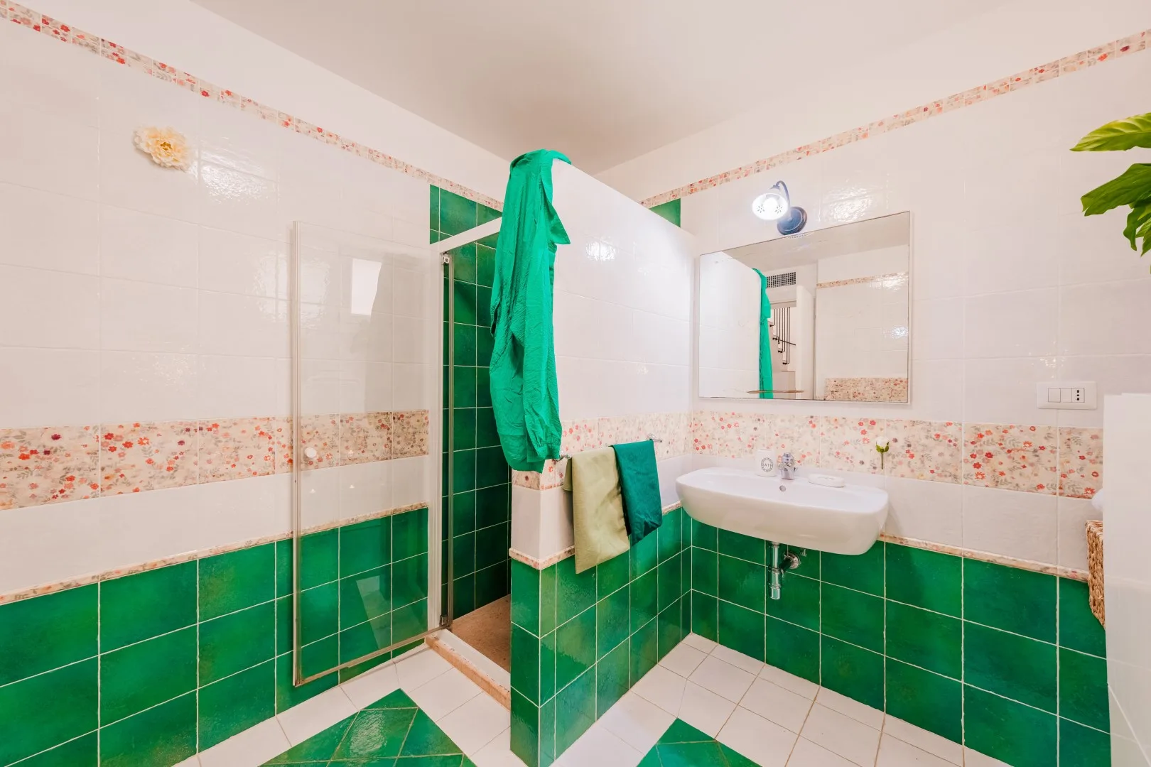 Un baño de azulejos con lavabo, espejo y paredes verdes y blancas.
