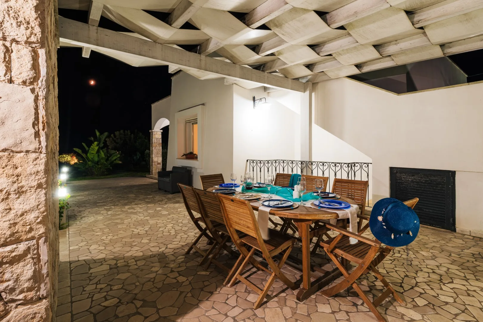 Comedor exterior cubierto con una mesa y asientos de madera, de noche.