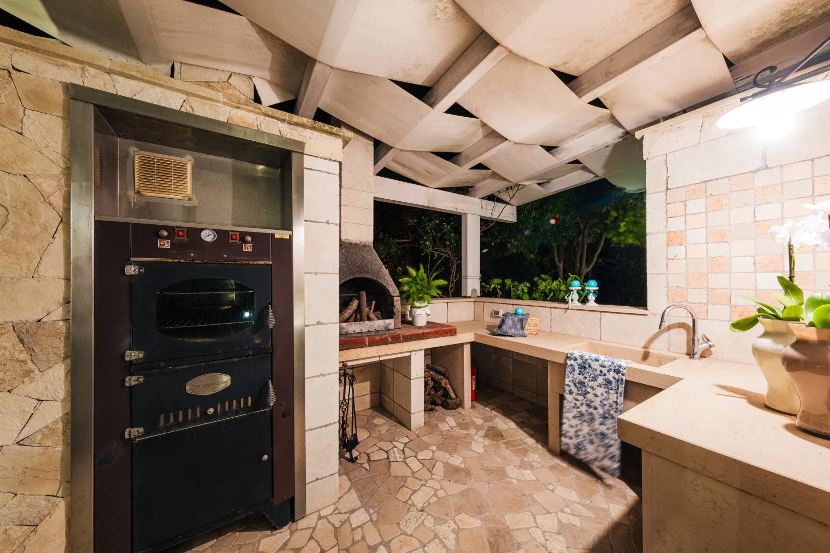 Una cocina exterior con horno empotrado, encimeras y suelo de piedra.