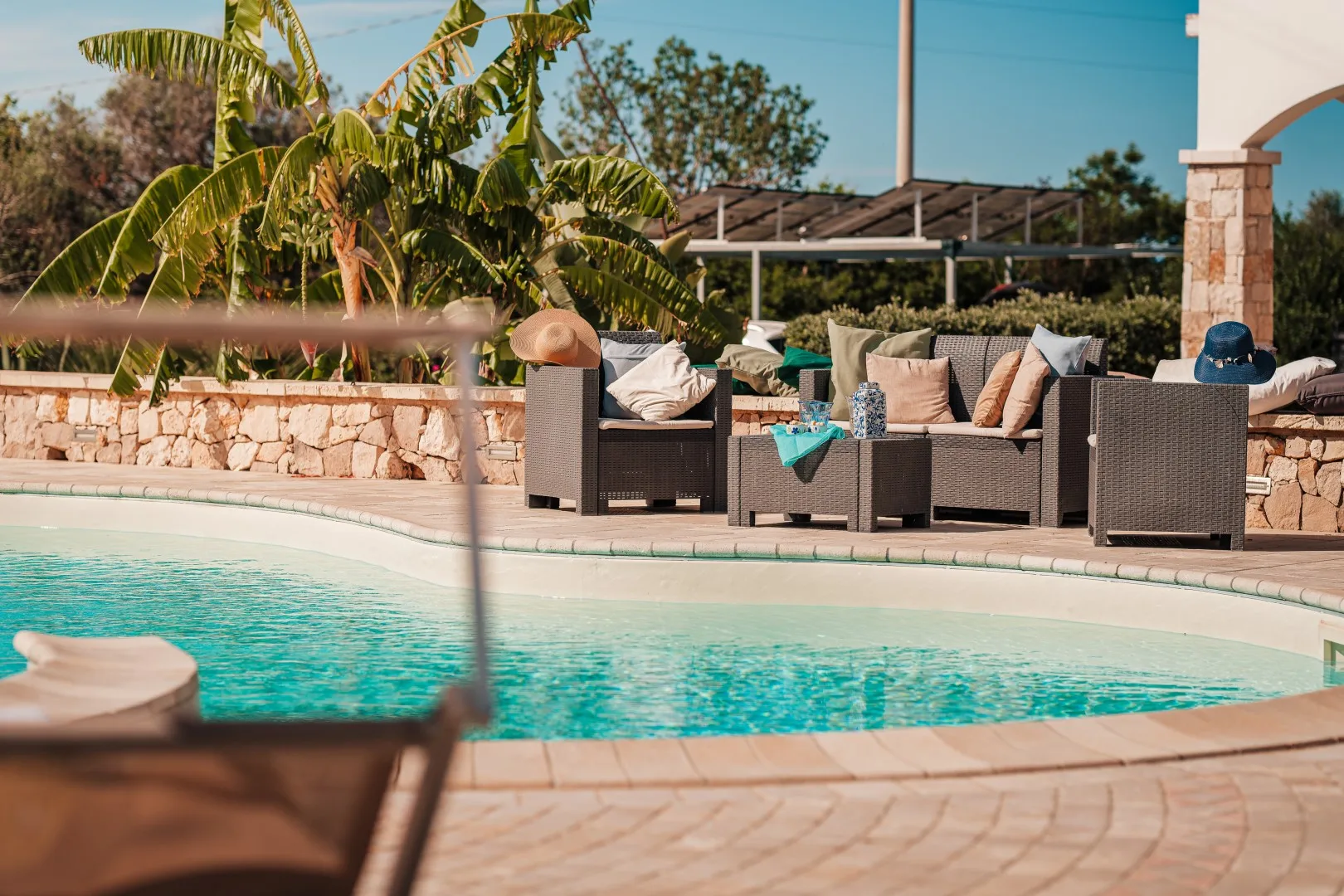 Una piscina al aire libre está rodeada de asientos acolchados y plantas tropicales.