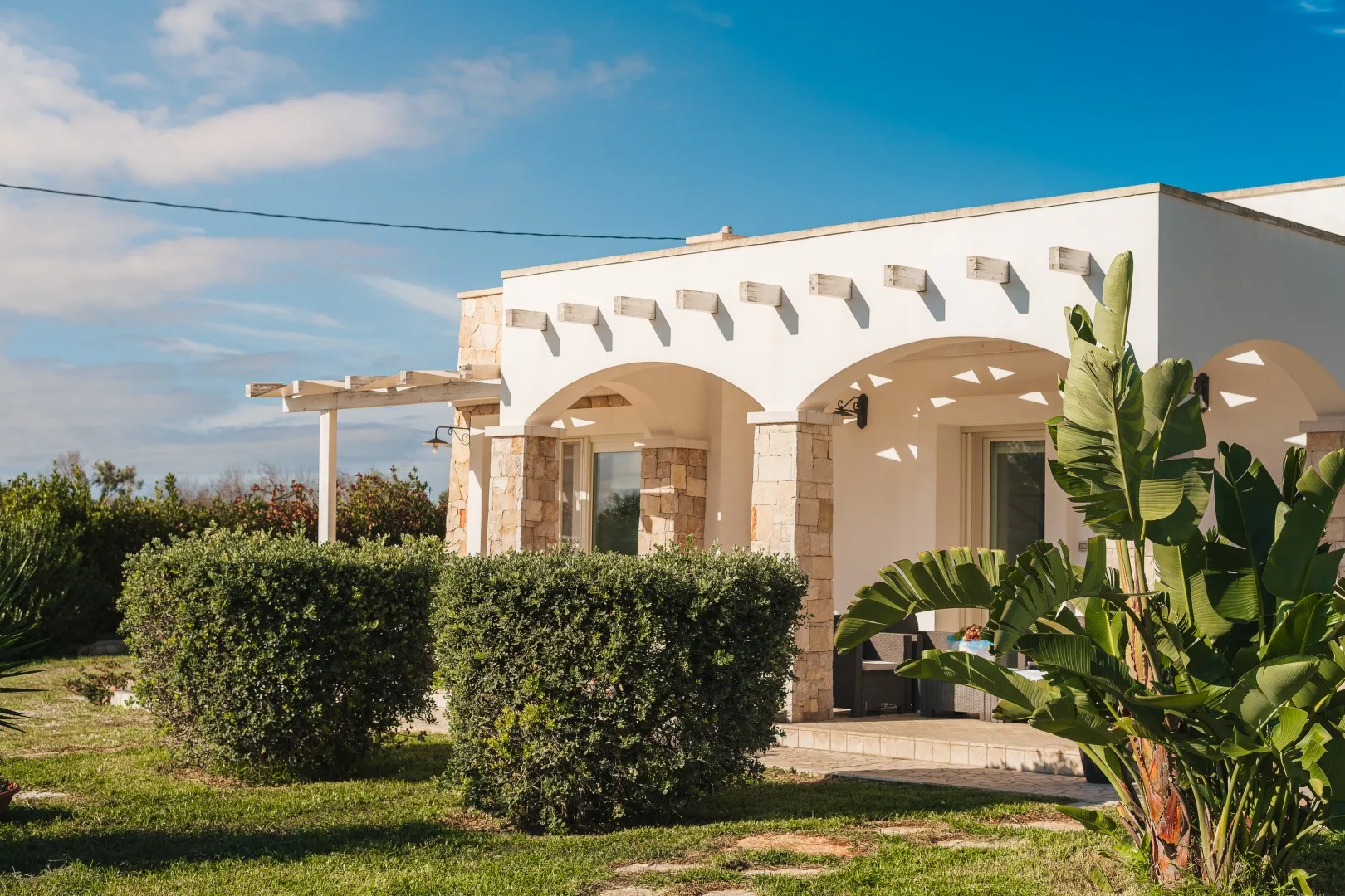 Una casa blanca con arcos se alza detrás de un seto de jardín.