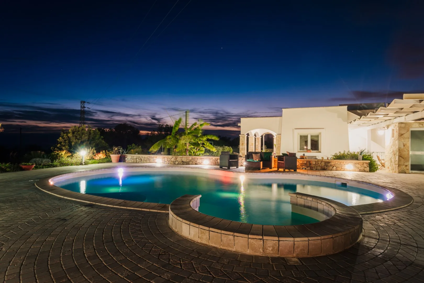 Una piscina al aire libre está junto a una casa moderna al anochecer.