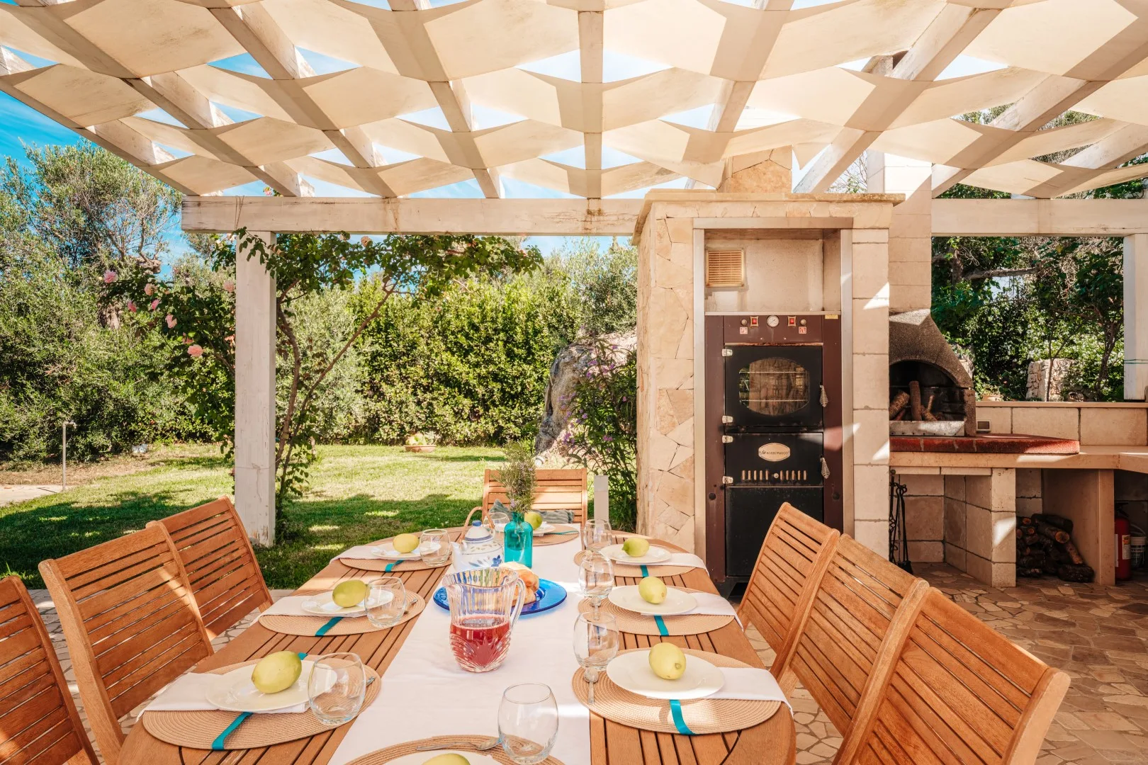 Comedor al aire libre bajo una pérgola, con una mesa y una zona de cocina.