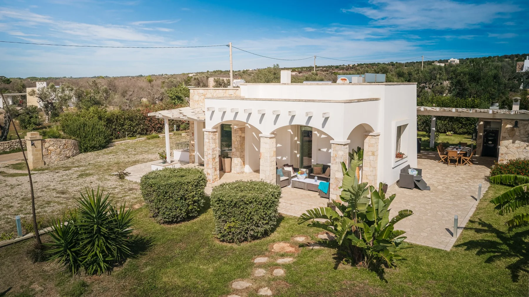 Una casa blanca con aberturas arqueadas se encuentra en un patio ajardinado.