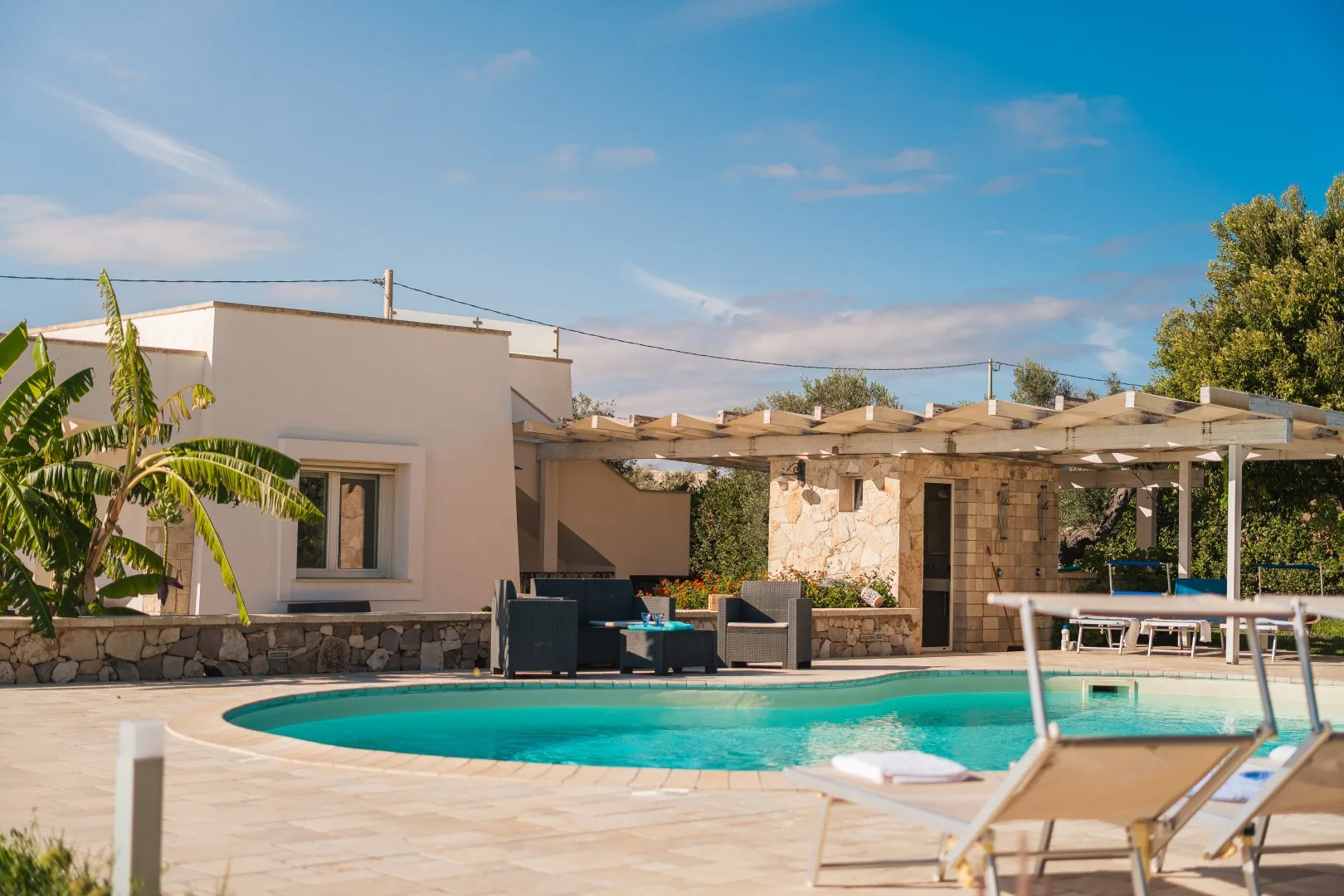 Piscina al aire libre junto a una zona de estar en un patio con pérgola.