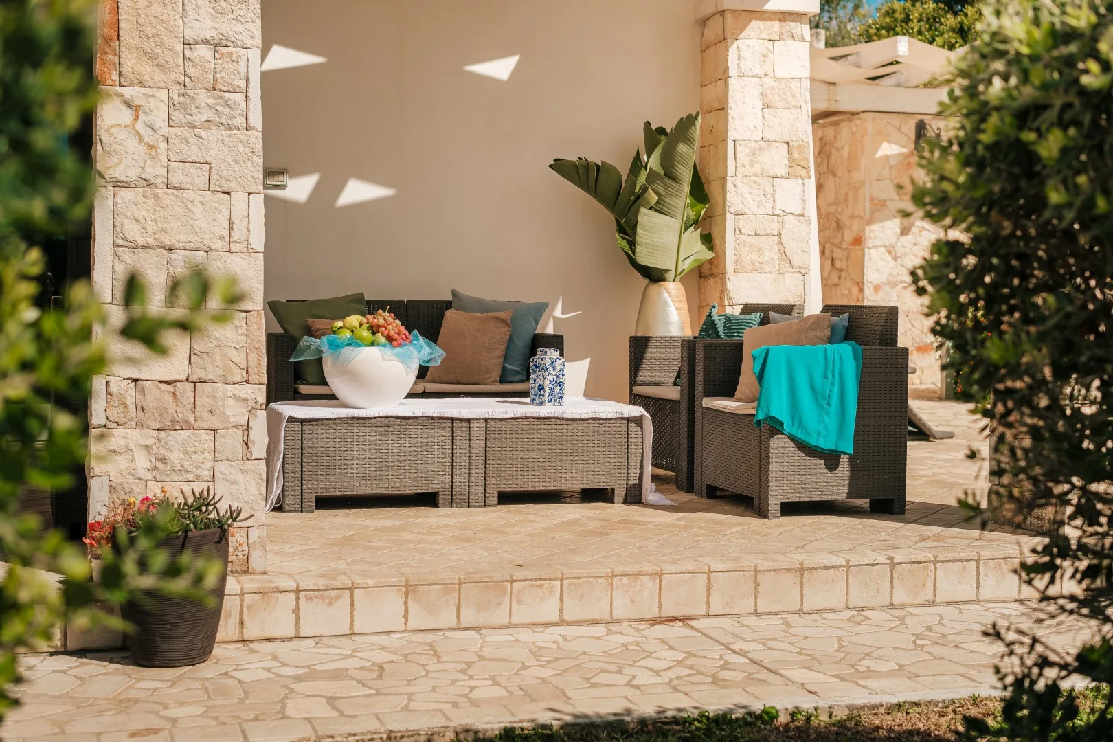Una zona de estar en un patio exterior con cojines y plantas en macetas.