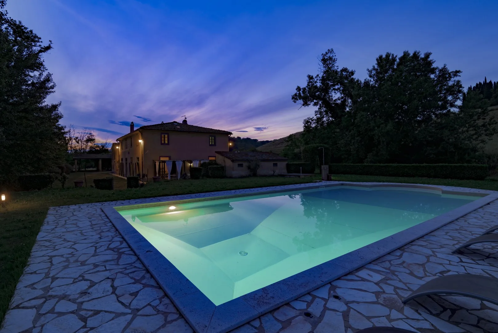 Una piscina iluminada está junto a una casa al anochecer.