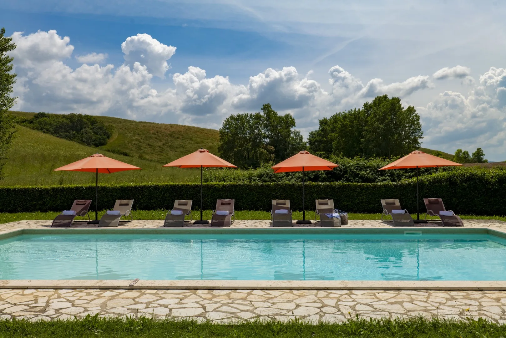 Una piscina al aire libre con asientos reclinables y sombrillas naranjas a su lado.