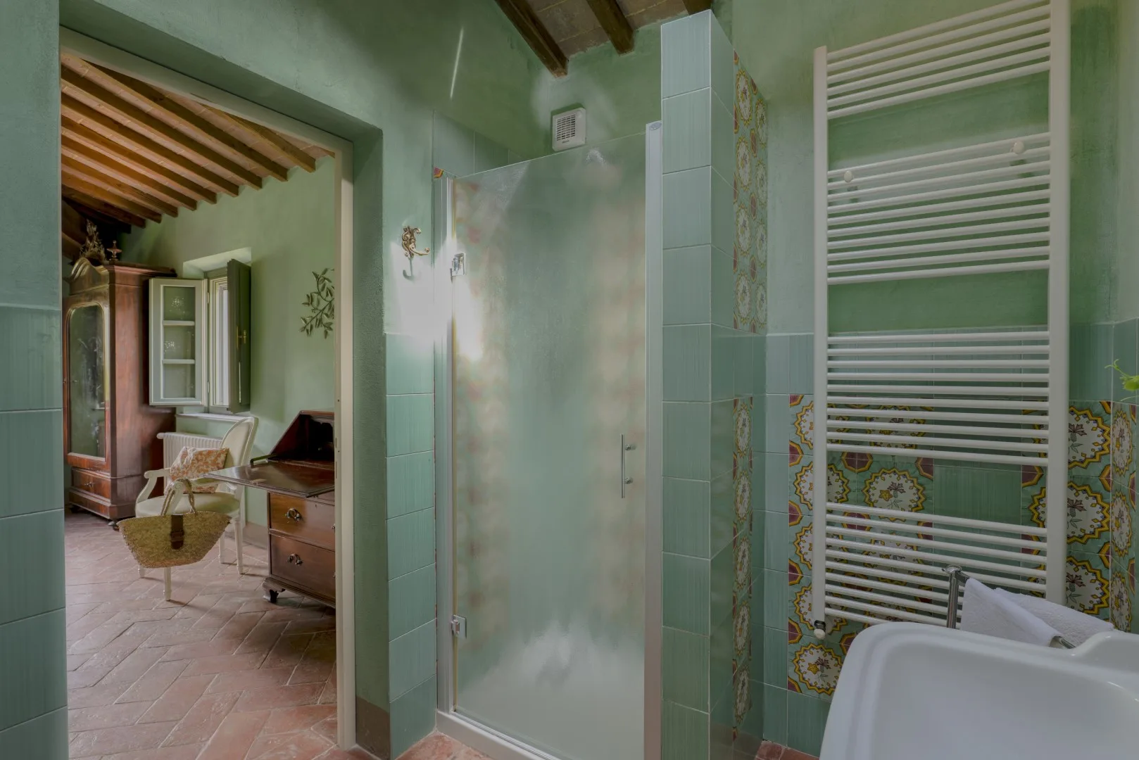 Un baño alicatado con una ducha de vidrio y un radiador toallero blanco.