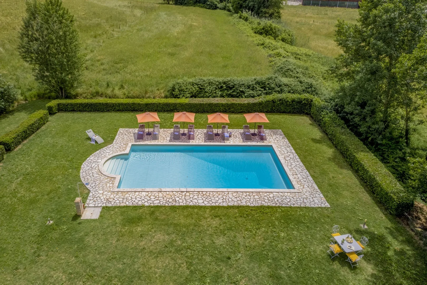 Una piscina está en una zona exterior con césped, con tumbonas y sombrillas cerca.