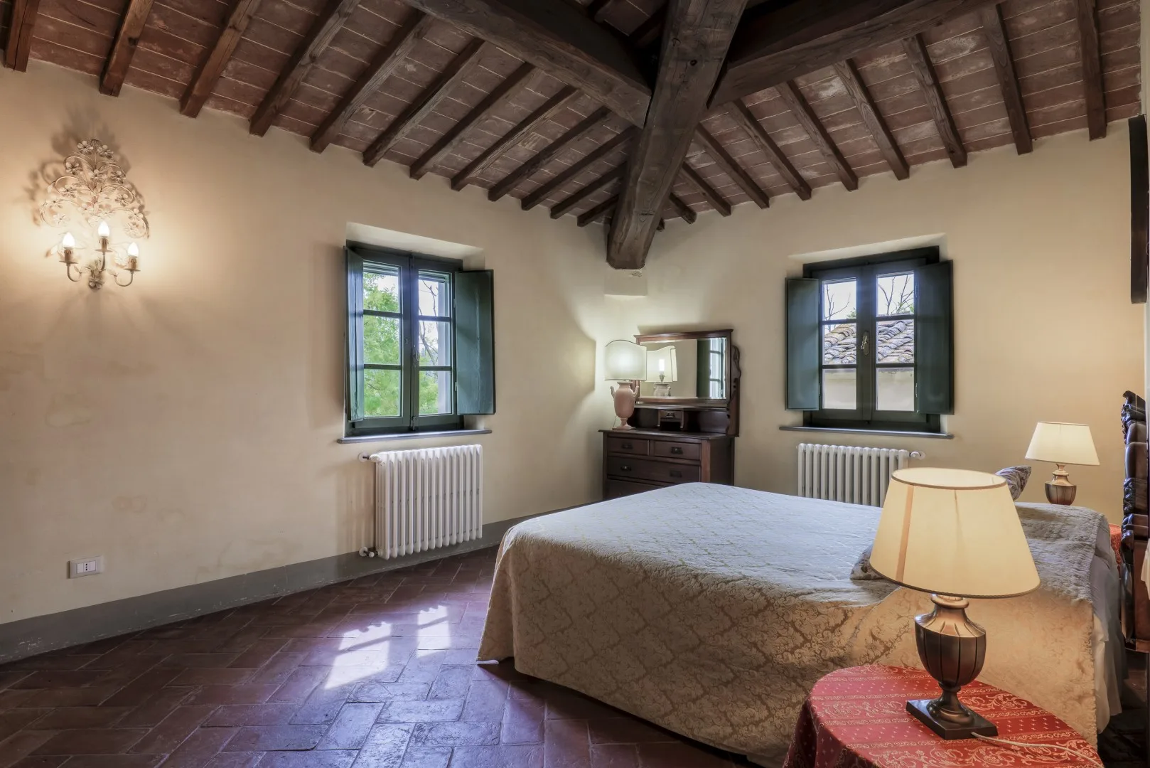Un dormitorio con una cama grande, dos ventanas y vigas de madera expuestas en el techo.