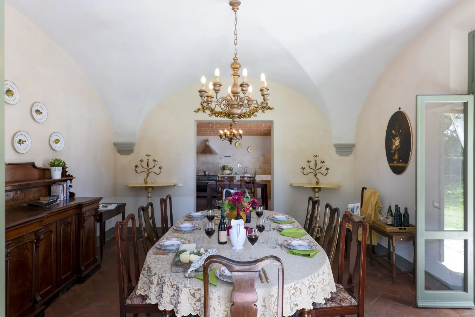 Un comedor con una mesa larga puesta con platos y flores bajo una lámpara de araña.