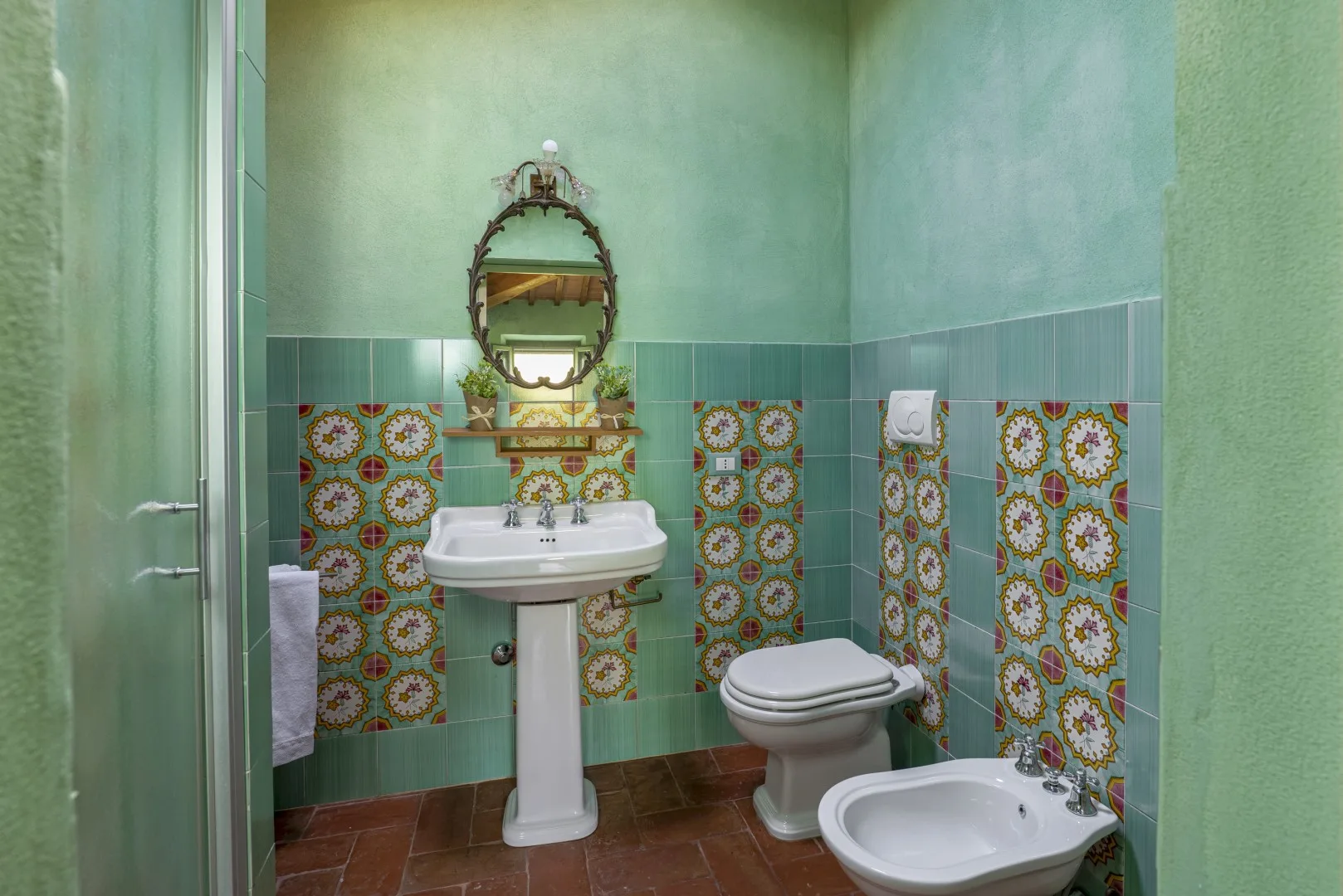Un baño alicatado con lavabo de pedestal, inodoro y azulejos decorativos.