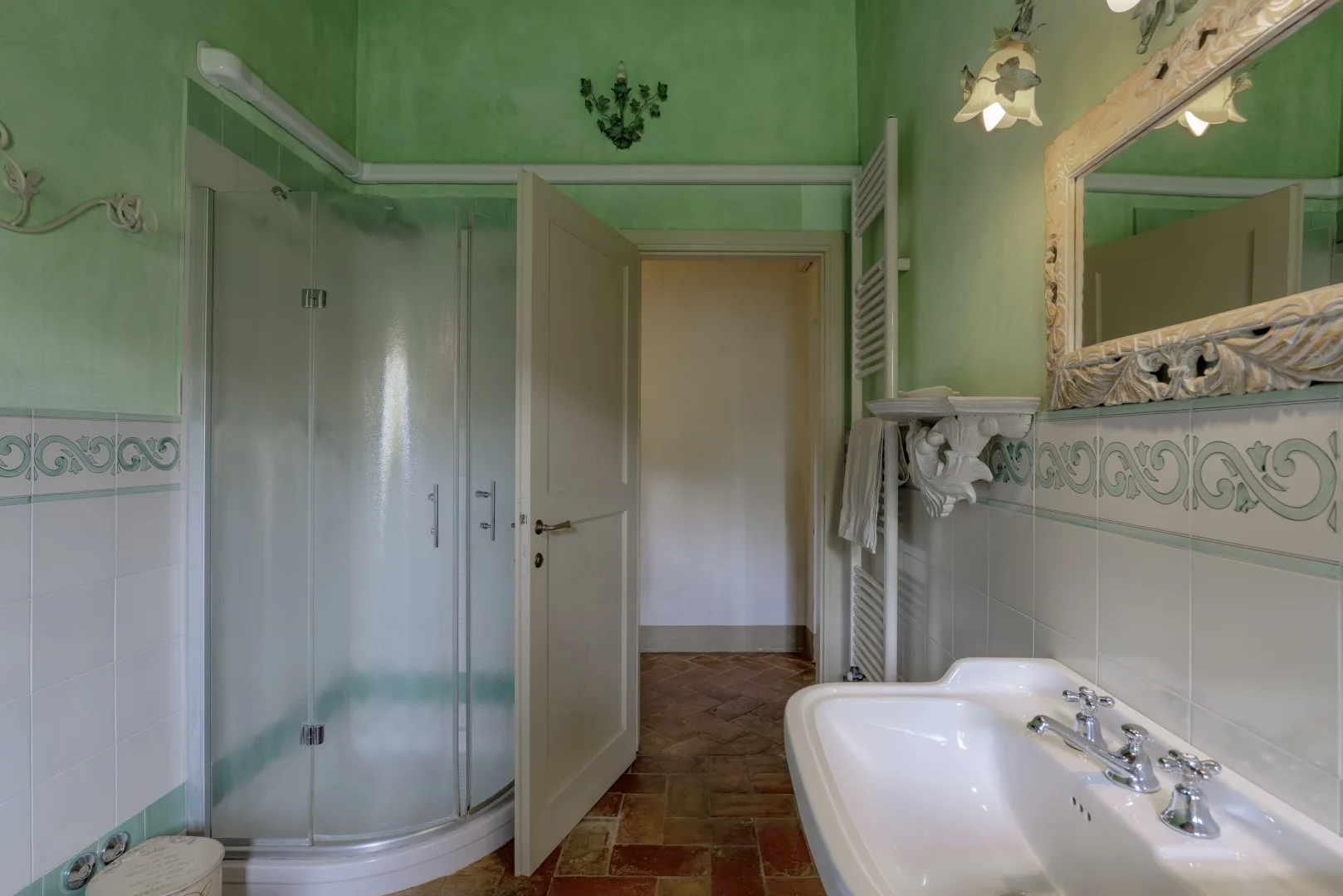 Un baño verde con una ducha de vidrio, un lavabo y un espejo decorativo.