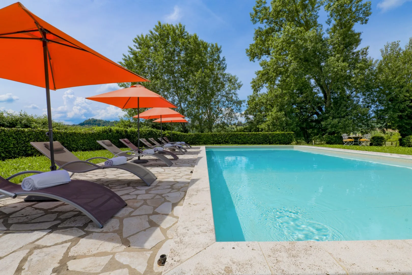 Una piscina al aire libre junto a tumbonas y sombrillas naranjas.