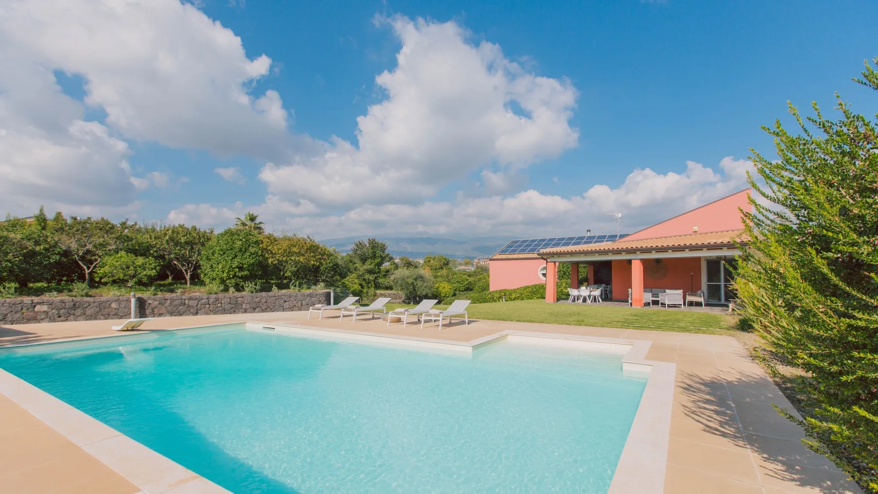 Una piscina al aire libre junto a un patio con asientos y un edificio bajo.