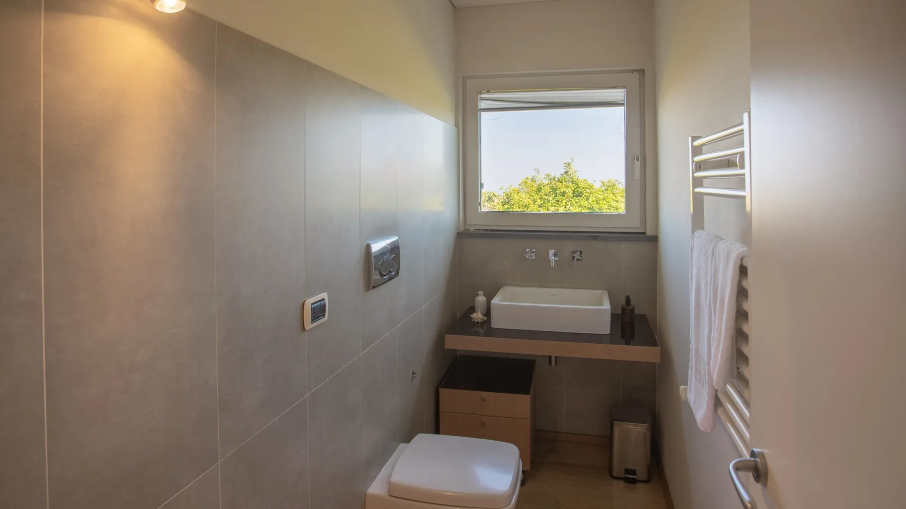 Un baño con paredes de azulejos, lavabo bajo una ventana e inodoro.