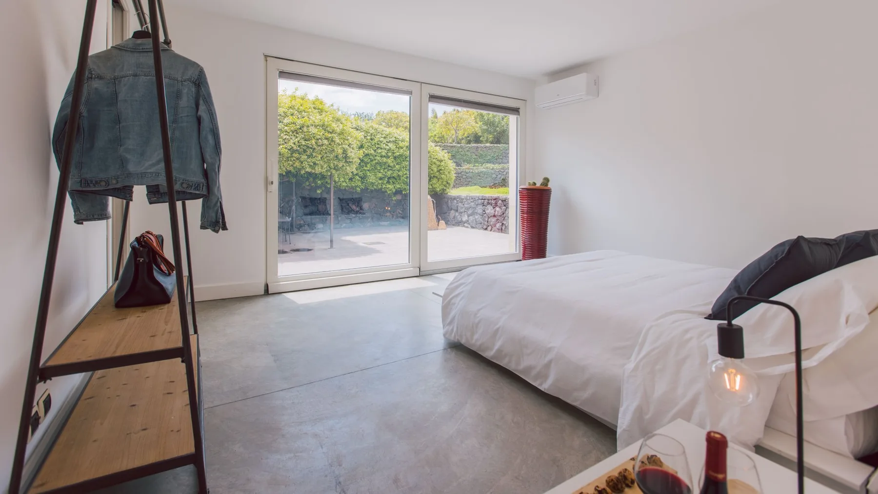 Un dormitorio luminoso con una cama baja junto a grandes puertas de vidrio que dan a un patio.